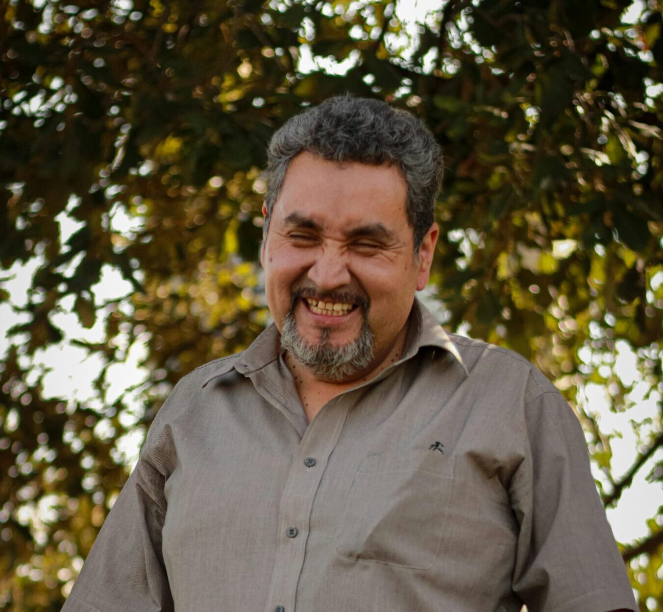 Happy man standing outdoors in casual clothes with trees in the background.