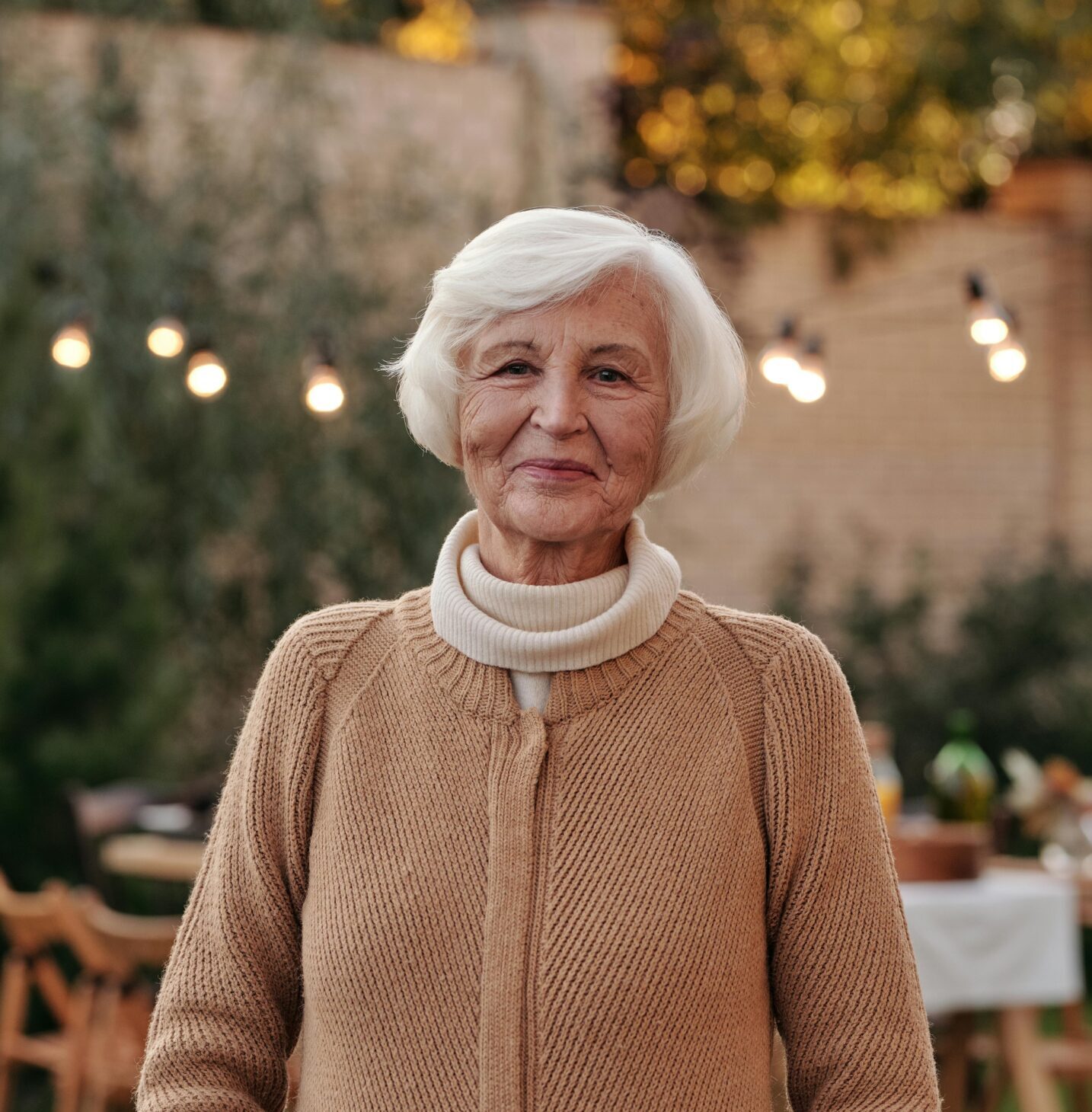 Cheerful senior woman in a cozy cardigan enjoying an outdoor gathering in the garden.